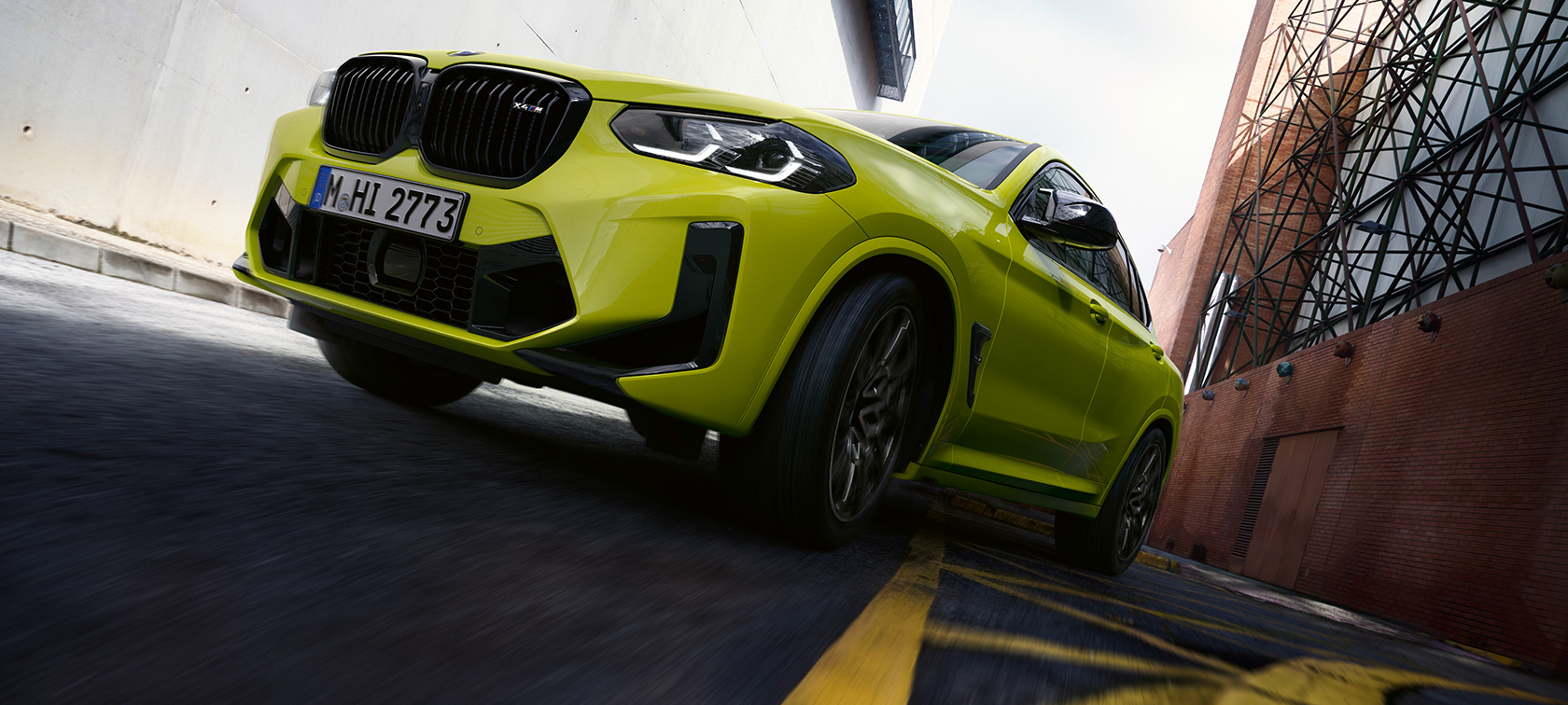 BMW X4 M Competition F98 LCI Facelift 2021 Sao Paulo Yellow Vista anteriore a tre quarti dal basso in movimento tra case